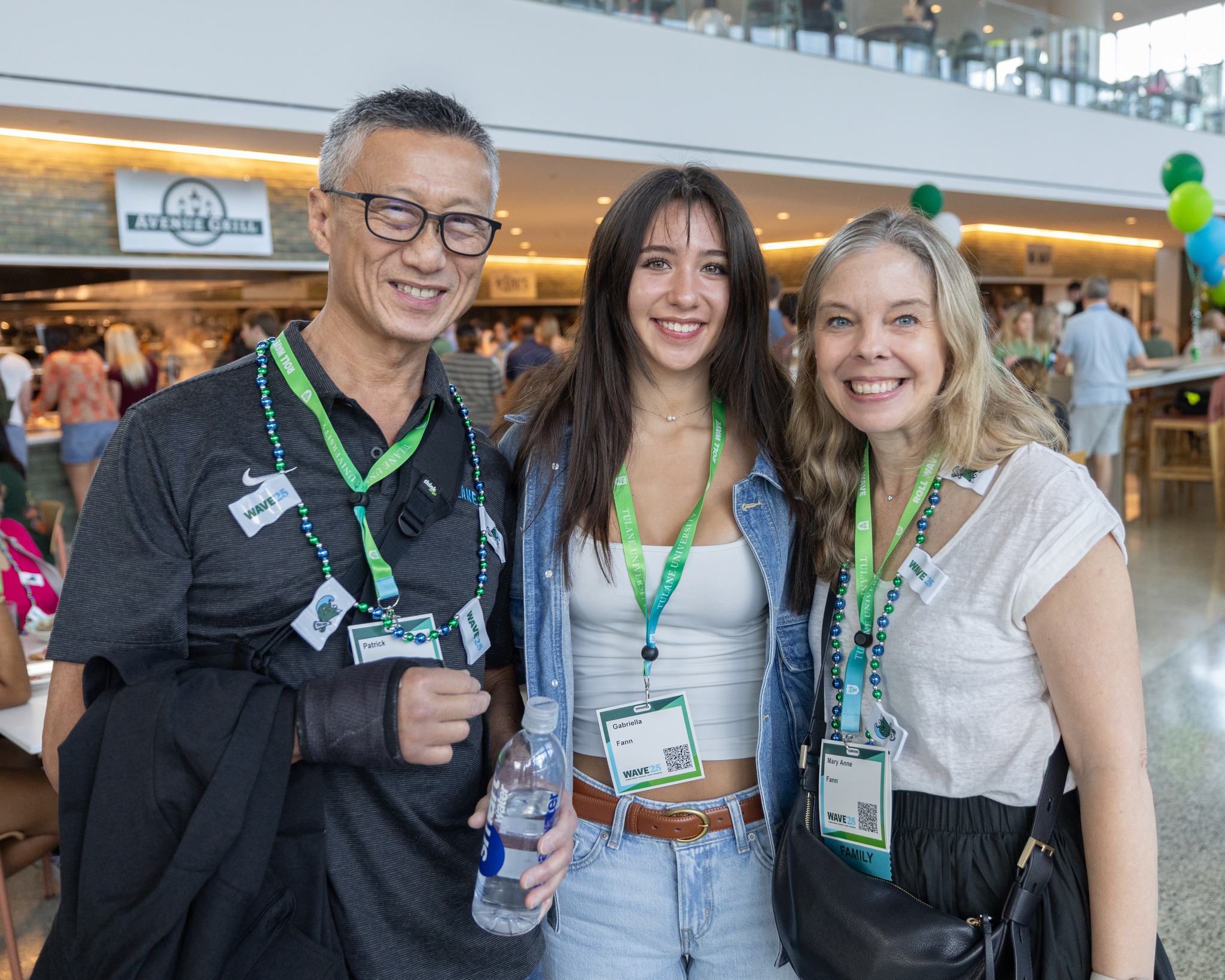 Smiling man in glasses and cast, young woman, and woman with lanyards at an indoor event.