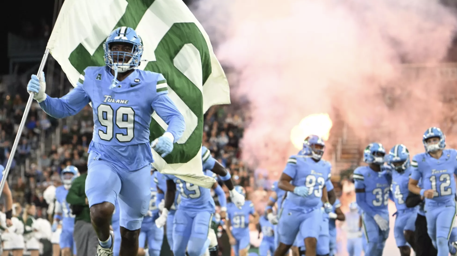 Photo: Football player #99 in light blue Green Wave jersey holds Devon Walker #18 flag, team runs onto field through smoke